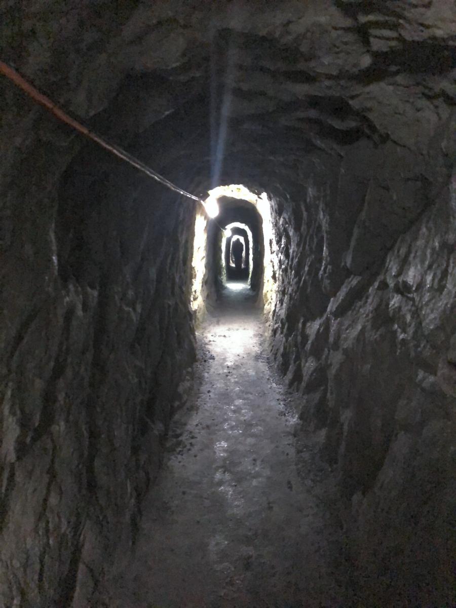 Chodba kamenné štoly, na konci je vidět světlo a před světlem stojí postava